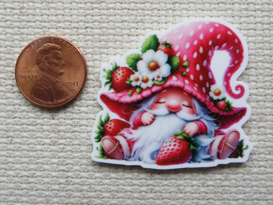 First view of an adorable sitting red gnome with a strawberry hat minder. The gnome is holding a strawberry and the hat has a small strawberry with white strawberry blossoms.